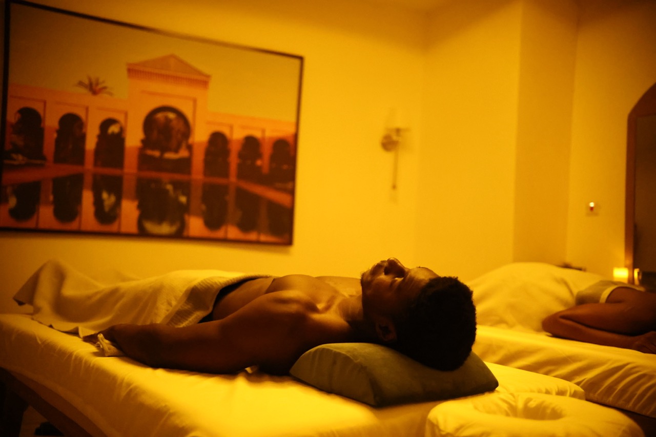 A man lying on a massage bed in a treatment room, Moroccan archway mural on the wall, candlelit warm tones