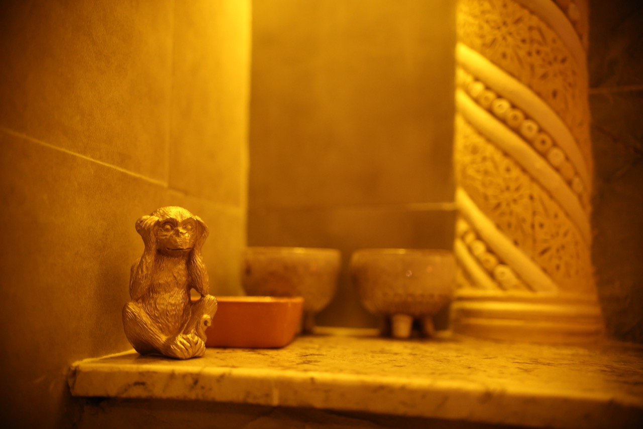 Detail of the GoldCat hammam: a small gold figurine on warm marble, ornate Moroccan carved column behind it, candlelit warm tones