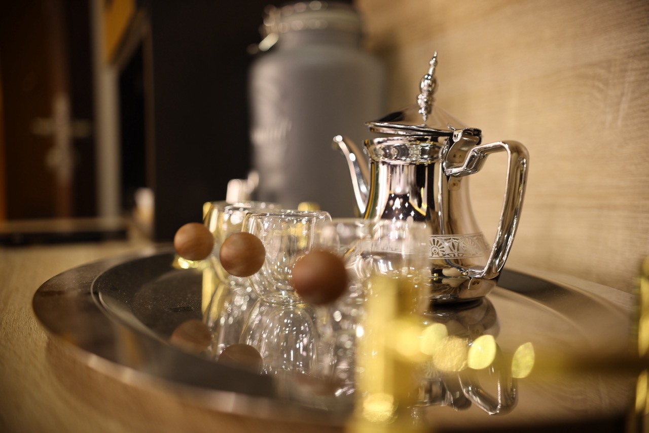 Close-up of an ornate silver Moroccan tea kettle on a tray with small tea glasses, candlelit warm interior