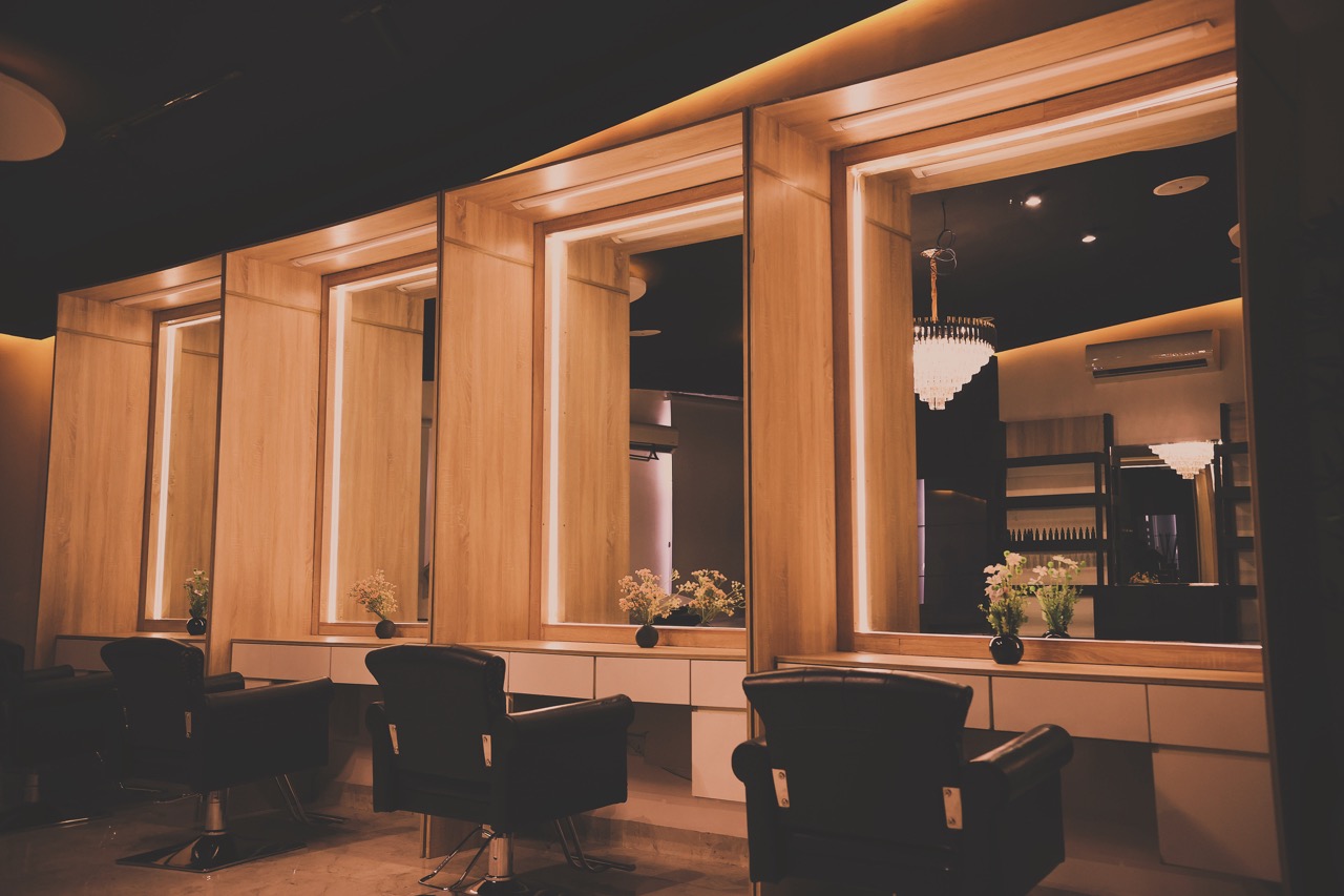 The GoldCat hair studio: three styling chairs facing tall LED-lit vanities, a chandelier, fresh flowers on each station